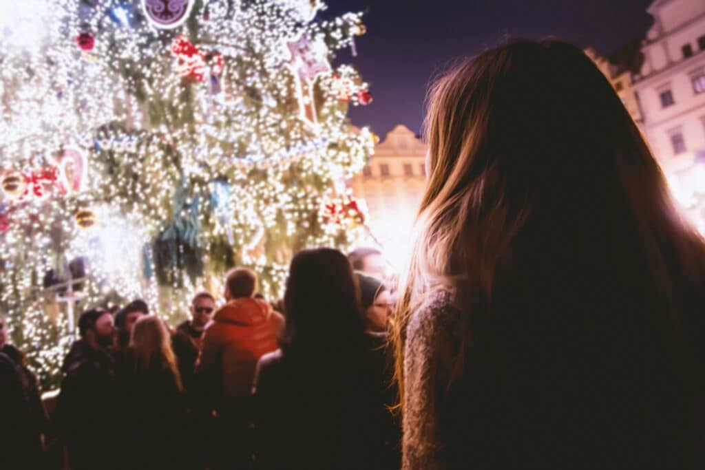 Vue arrière d'une femme aux cheveux longs regardant un grand marché de Noël illuminé par des milliers de lumières scintillantes.